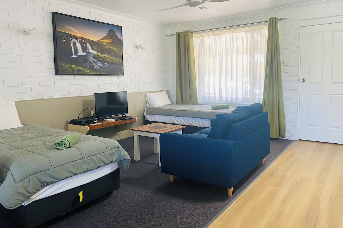 A hotel room with a bed, a sofa, a TV, and a window with curtains.