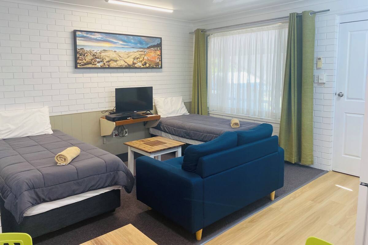 A compact room with two beds, a TV, a small table, and a sofa.