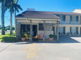 A motel with a covered entrance, outdoor seating, and a signboard.