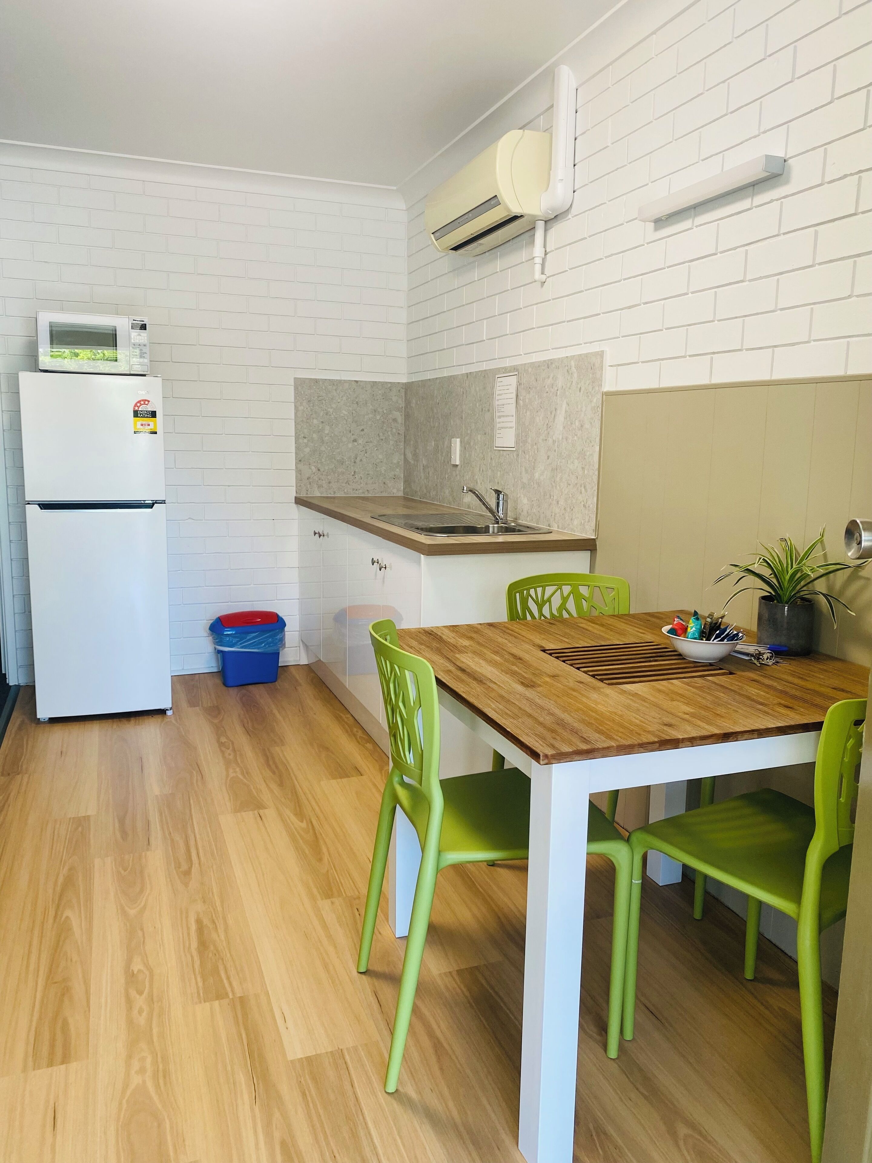 A compact kitchen with a microwave, refrigerator, sink, and a small dining area with a wooden table and green chairs.