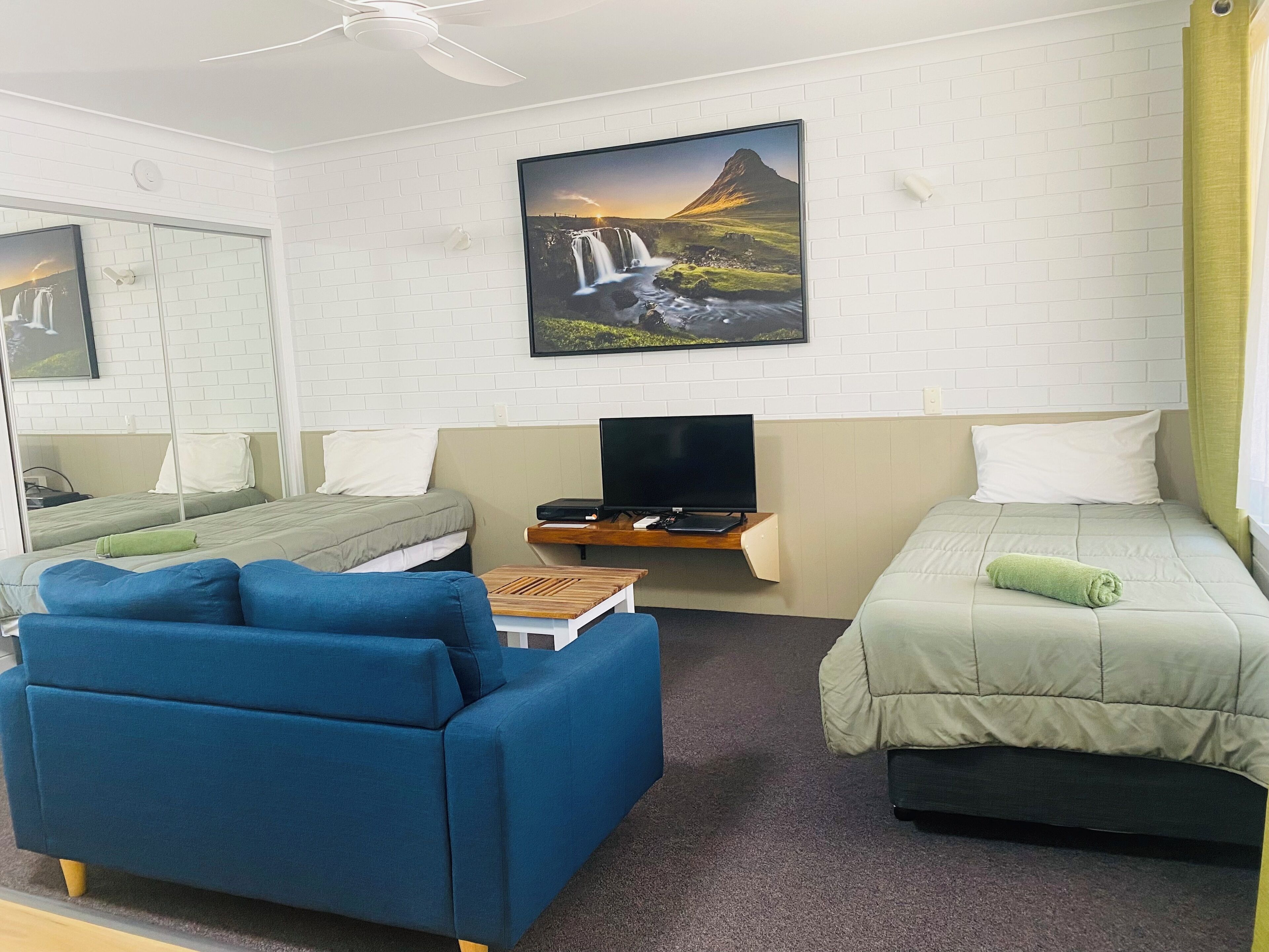 A hotel room with a bed, a sofa, a TV, and a painting of a waterfall.