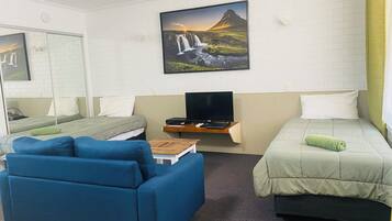 A hotel room with a bed, a sofa, a TV, and a painting of a waterfall.