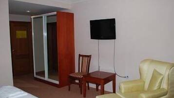 A hotel room with a bed, a wooden chair, a yellow armchair, a television mounted on the wall, and a sliding door.