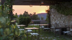 An outdoor seating area with tables and chairs, surrounded by greenery and a stone wall. - Castello di Petrata (Assisi)