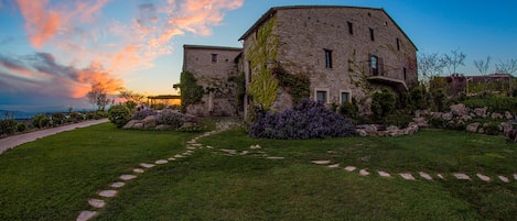 A stone building with a garden path leading to it, surrounded by greenery and rocks.