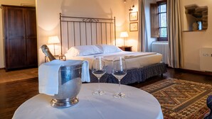 A hotel room with a bed, bedside lamps, a large window with curtains, a wooden ceiling, and a rug. - Castello di Petrata (Assisi)