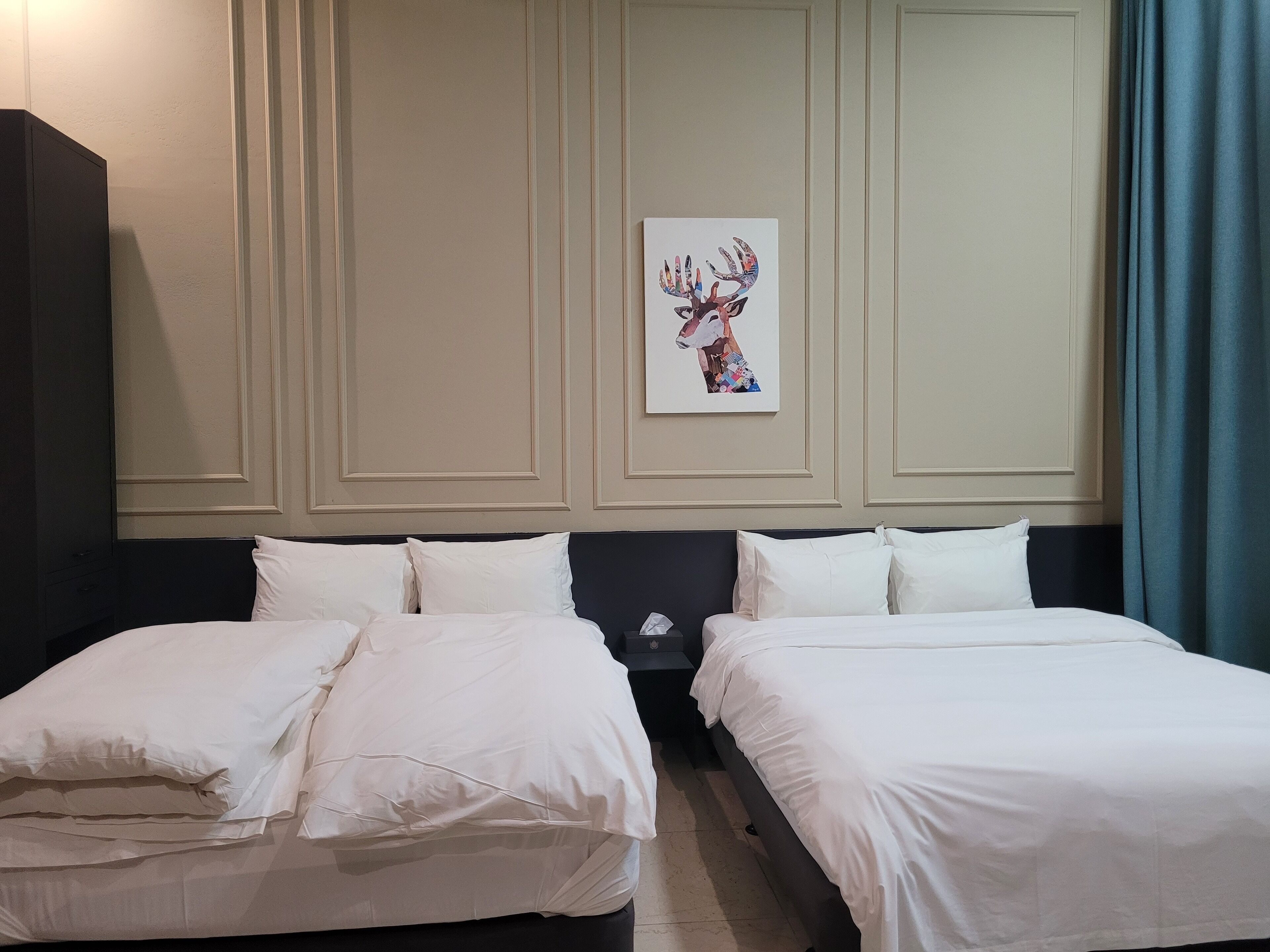 Quarto de hotel com duas camas, um quadro grande de um veado na parede e uma cortina azul.