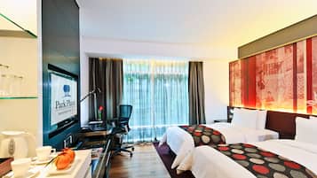 Habitación de hotel con escritorio, dos camas, televisor y un ventanal grande con cortinas.