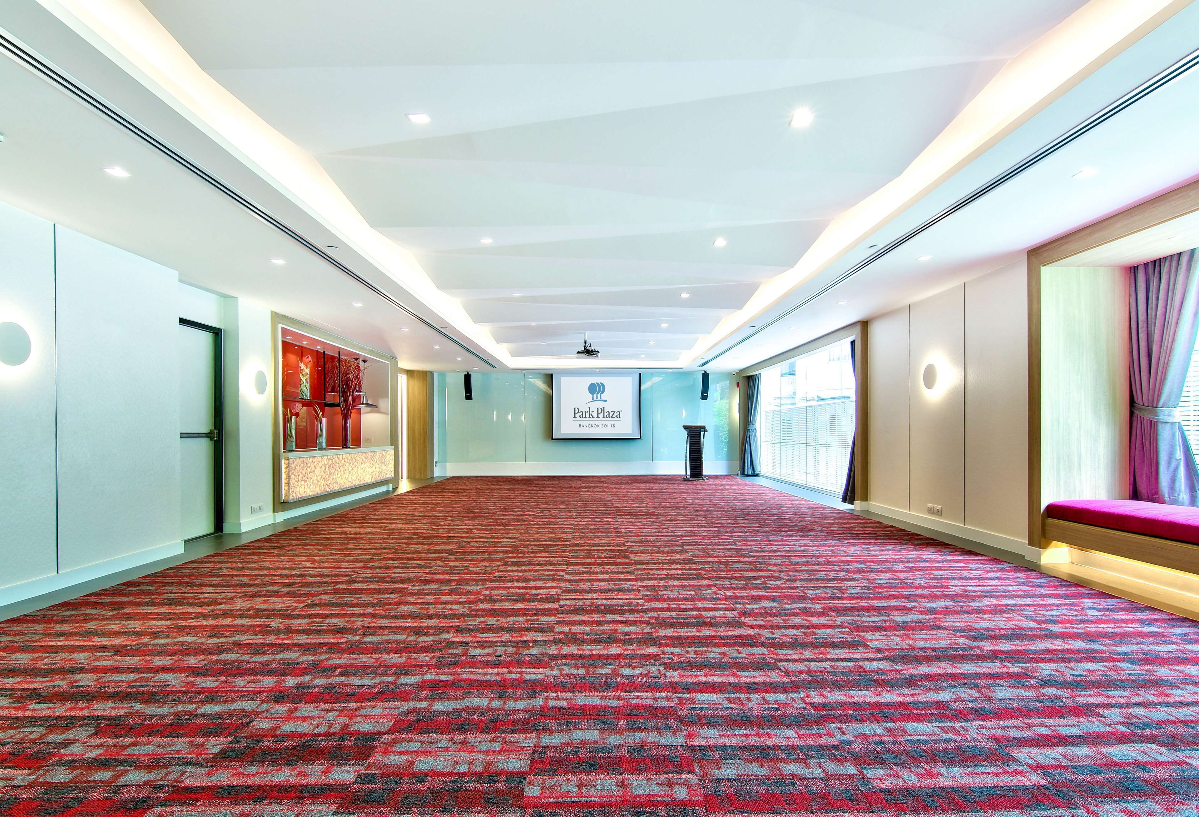 A spacious conference room with a red carpet, a large screen displaying 'Park Plaza', and a seating area with a pink bench.