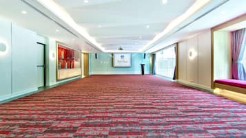 A spacious conference room with a red carpet, a large screen displaying 'Park Plaza', and a seating area with a pink bench.