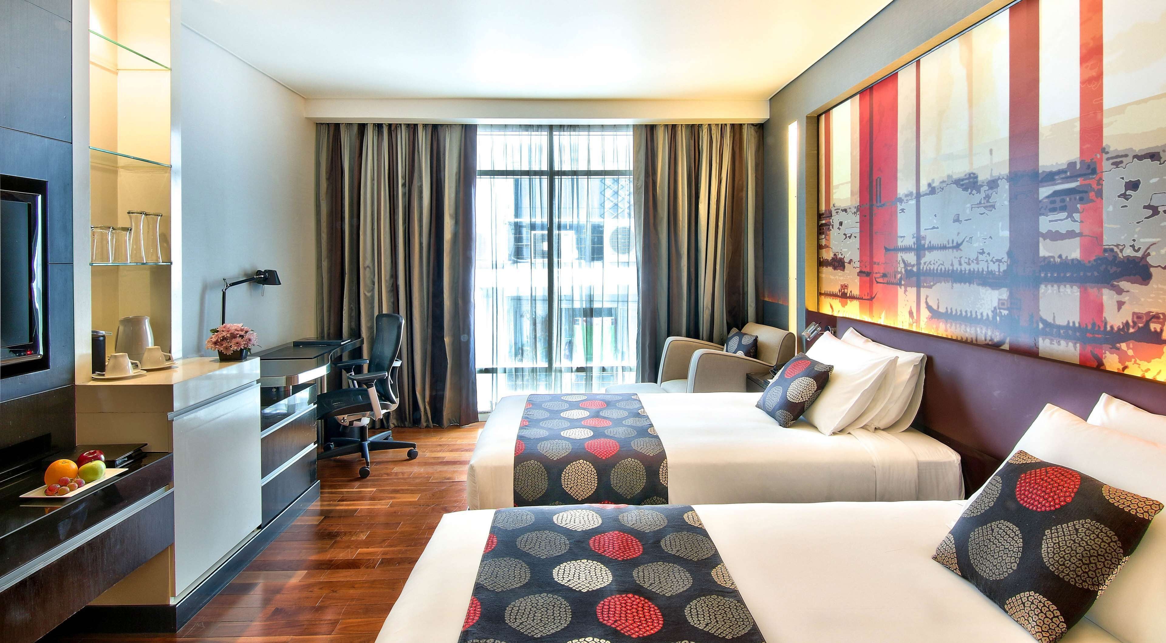 A hotel room with two beds, a desk, a television, and a large window with curtains.