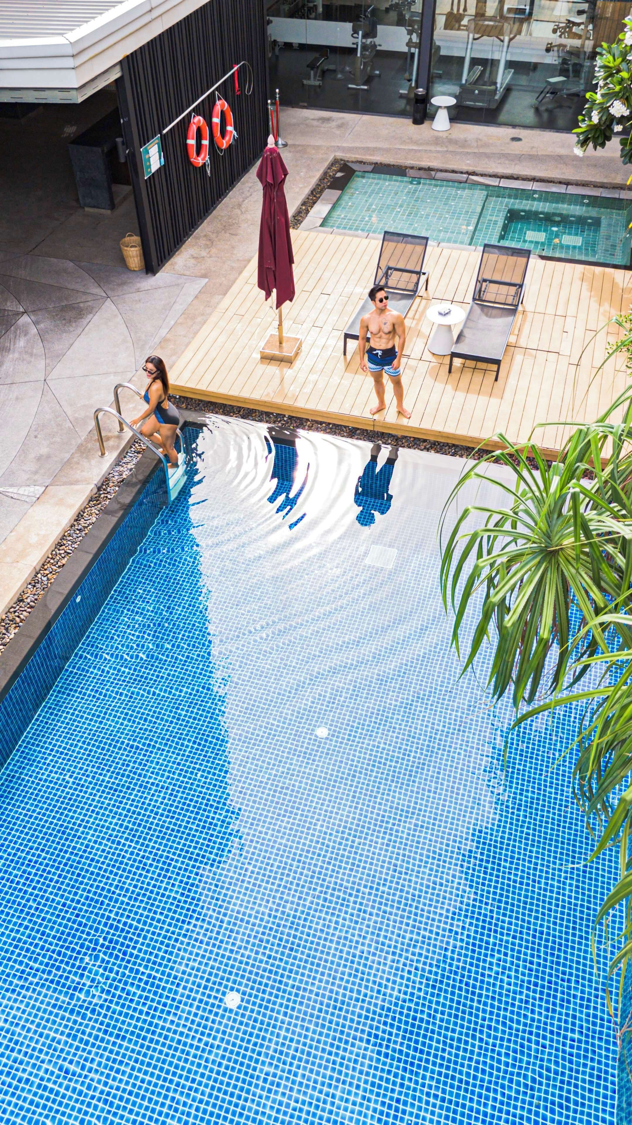 Una piscina con plataforma de azulejos, sillas de descanso y un flotador.