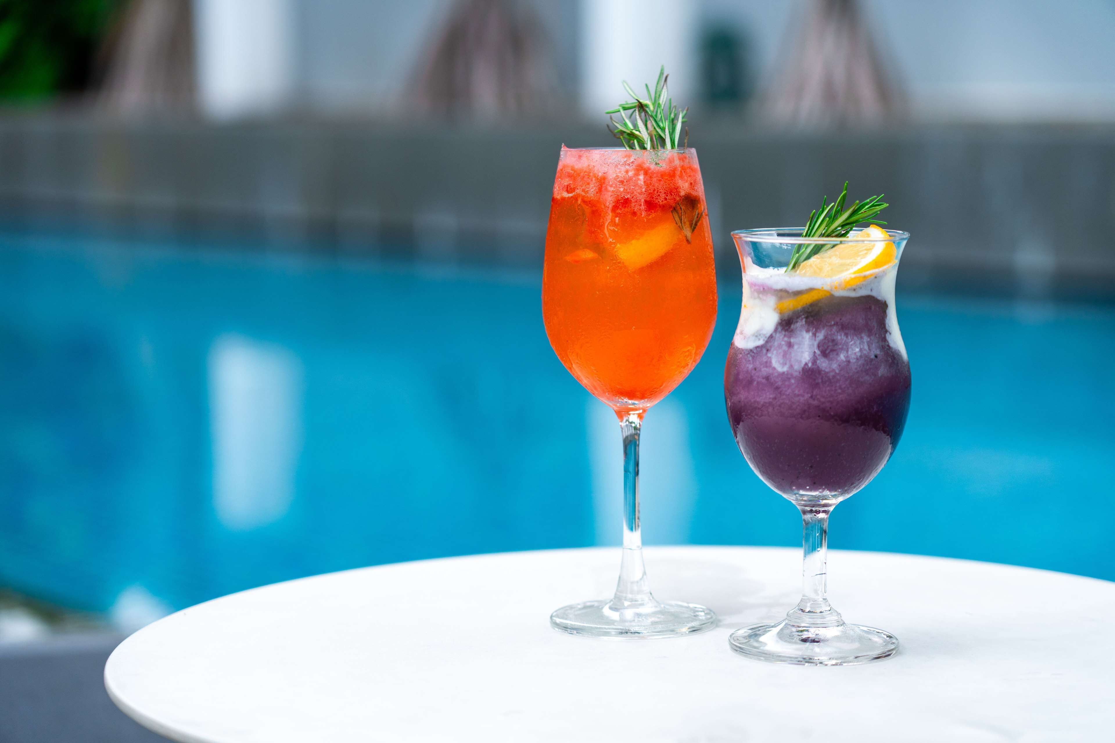 Two cocktails on a white table by a pool.