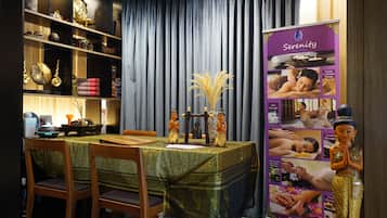 A dining area with a table set for two, a decorative vase, and a poster advertising Serenity Massage.