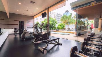 A modern gym with cardio machines, weightlifting equipment, and a large window overlooking a cityscape.
