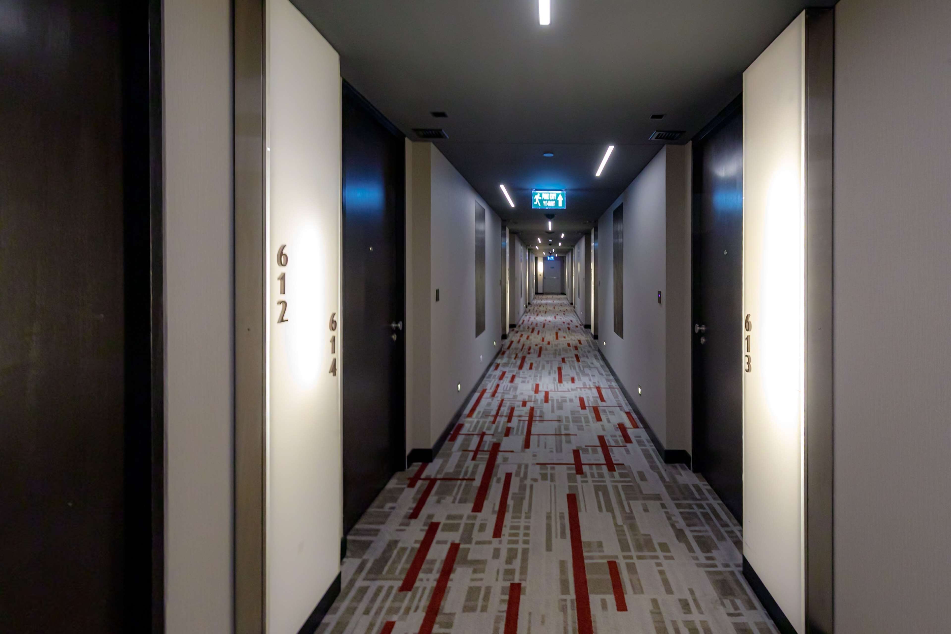 A hotel corridor with a patterned carpet, doors numbered 612 and 613, and a directional sign overhead.