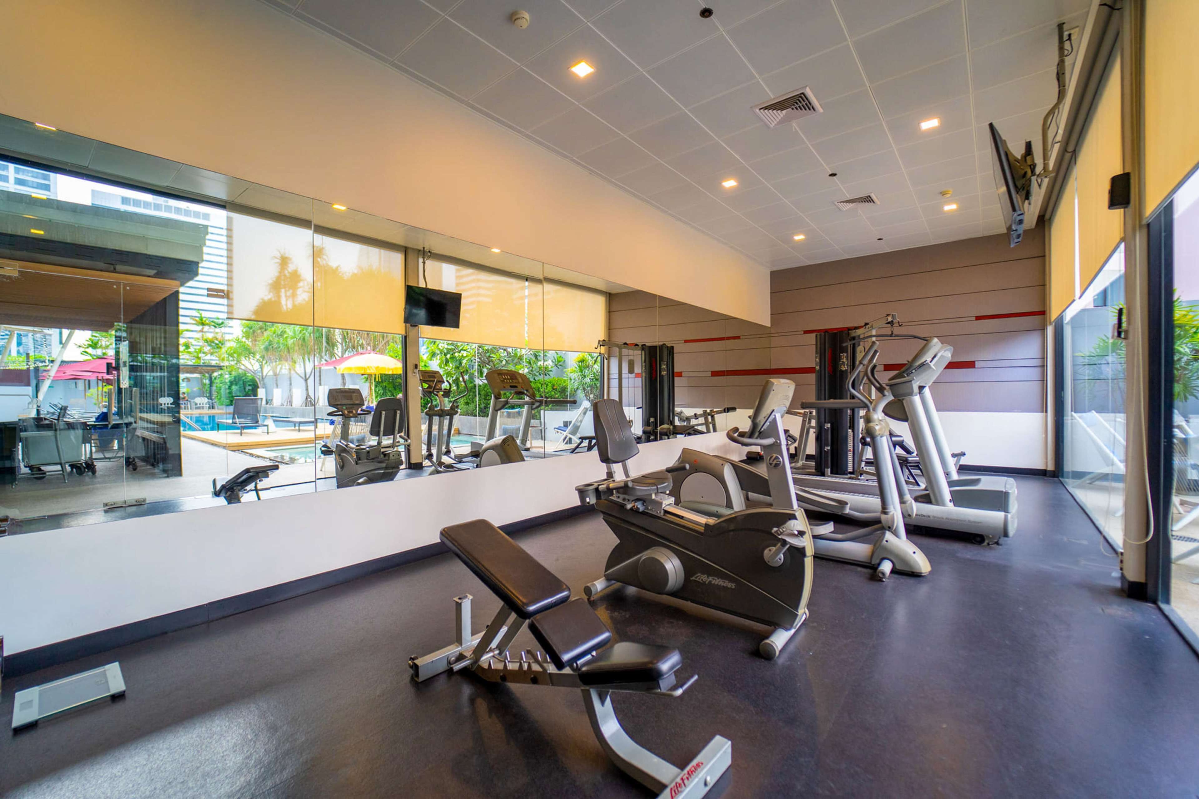 Ein modernes Fitnessstudio mit unterschiedlichen Trainingsgeräten, großen Fenstern und Blick ins Freie.