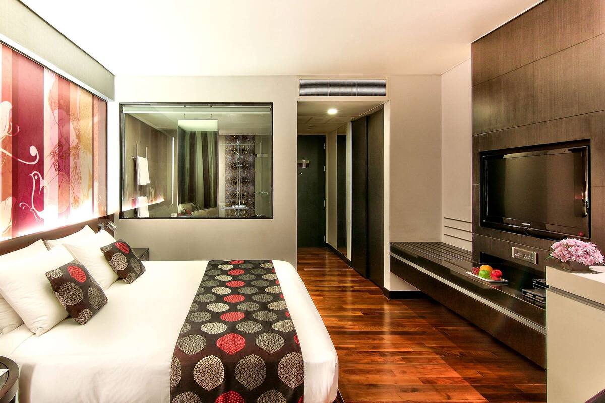 A modern hotel room with a large bed, a TV, a mirror, and a wooden floor.
