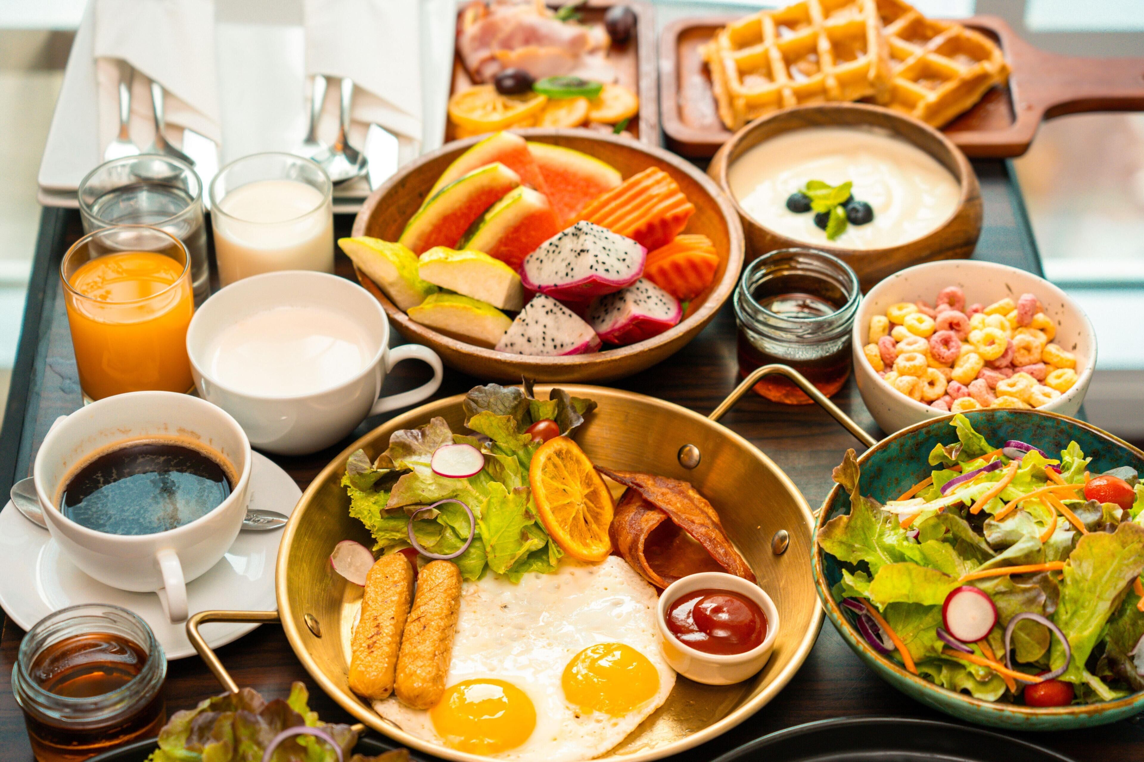 A breakfast tray with eggs, bacon, toast, fruit, cereal, and beverages.