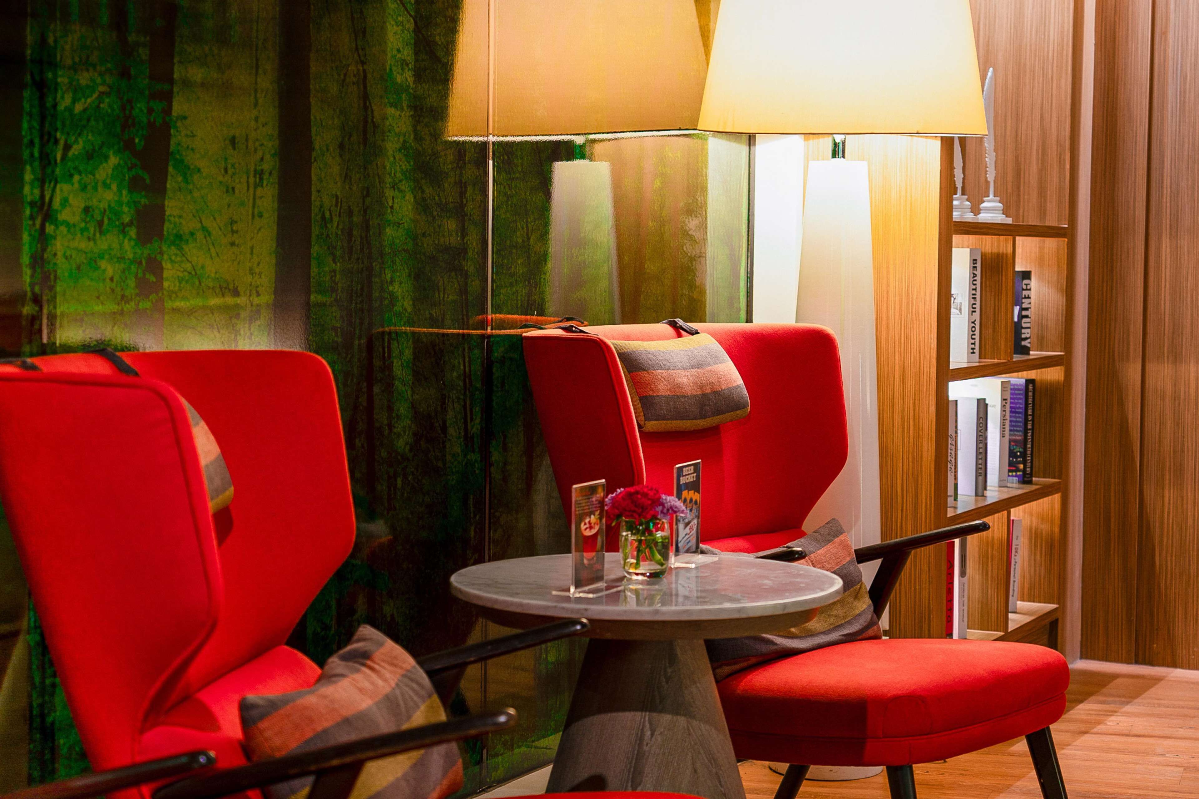 A modern room with two red chairs, a round table, a lamp, and a bookshelf with books.