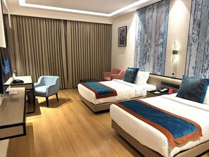 Une chambre d’hôtel avec deux lits, un bureau, une chaise, une télévision et une grande fenêtre avec des rideaux.