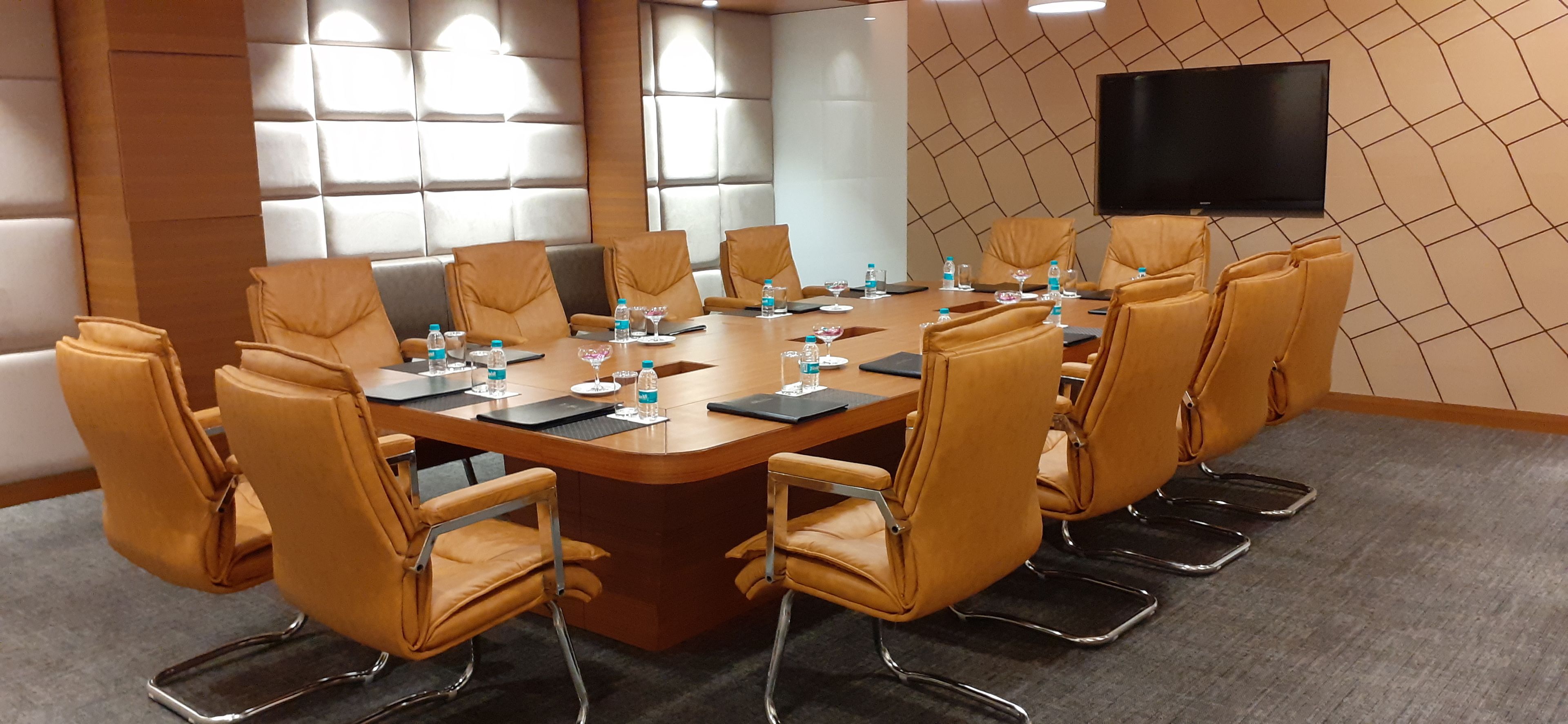 A conference room with a large table, multiple chairs, water bottles, glasses, and a flat-screen TV on the wall.