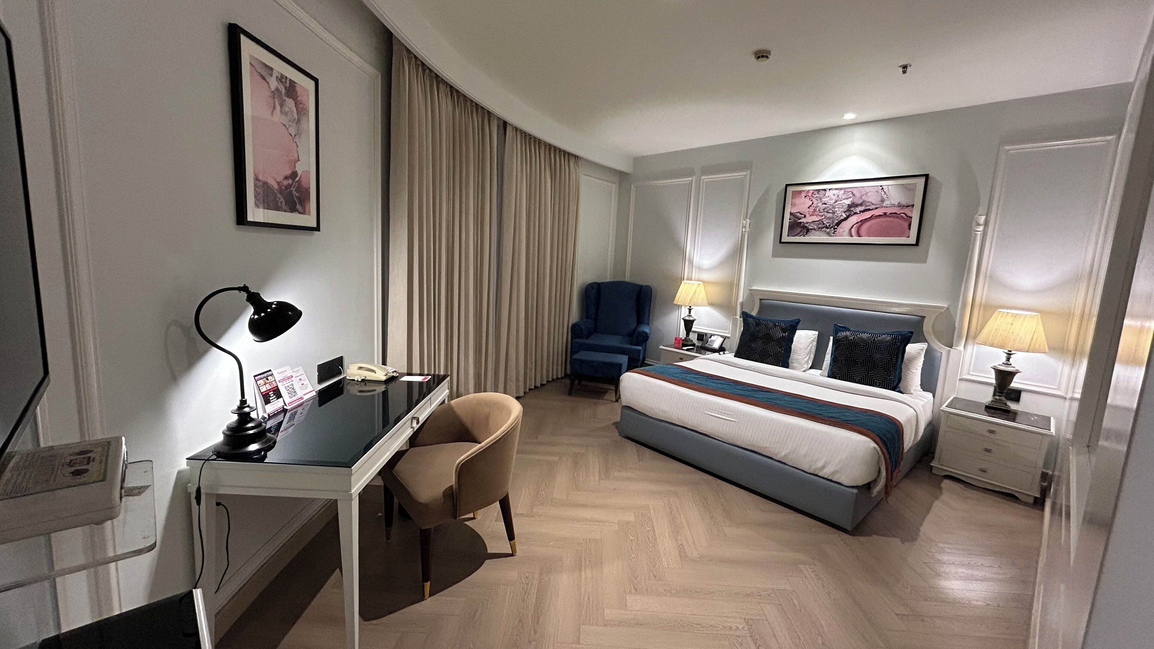 Une chambre d’hôtel comprenant un lit, un bureau, une chaise et deux tables de chevet avec des lampes.