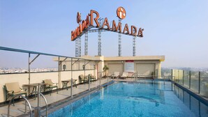 Een dakterraszwembad met uitzicht over de stad, ligbedden en een bordje met de tekst 'Ramada'.