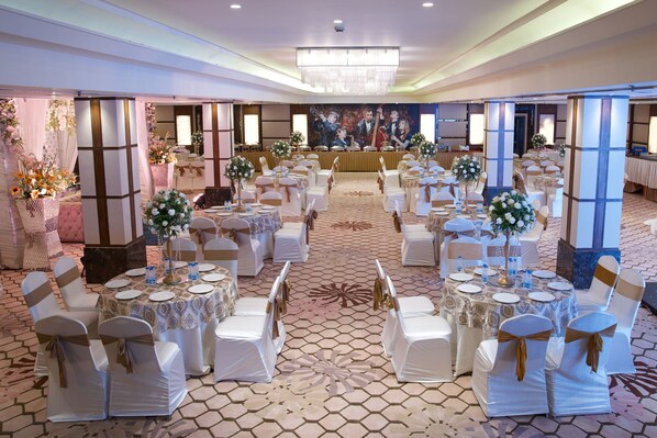 A banquet hall with round tables, white chairs, and floral centerpieces.