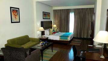 A hotel room with a bed, a green sofa, a desk with a lamp, and a TV on the wall.
