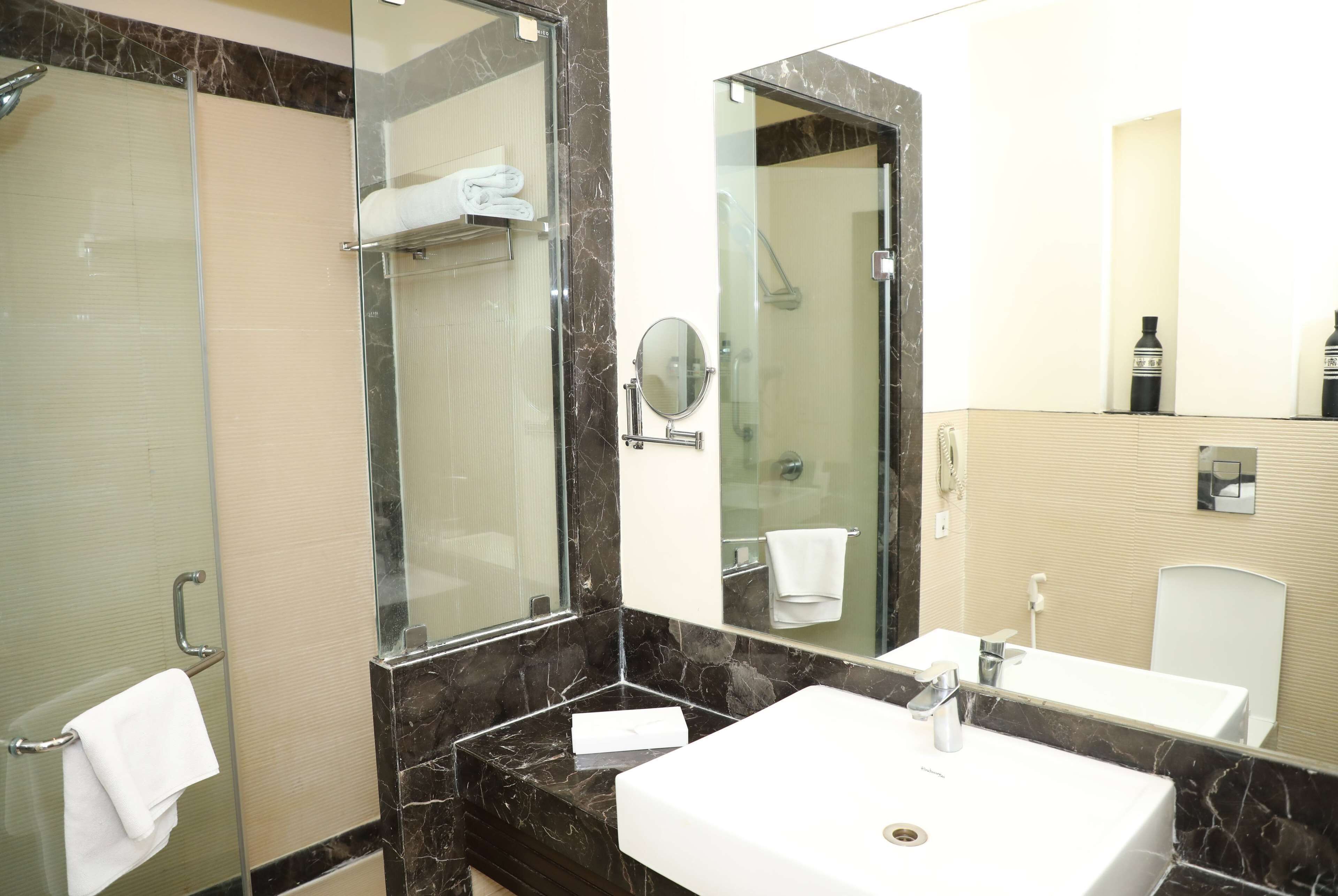 Un baño moderno con ducha envuelta en vidrio, un lavamanos blanco y un espejo grande.