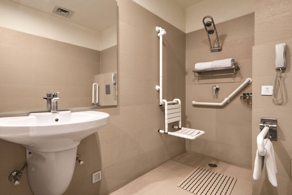Une salle de bain équipée d’un lavabo, d’une douche avec une barre d’appui, d’un porte-serviettes et d’un téléphone.