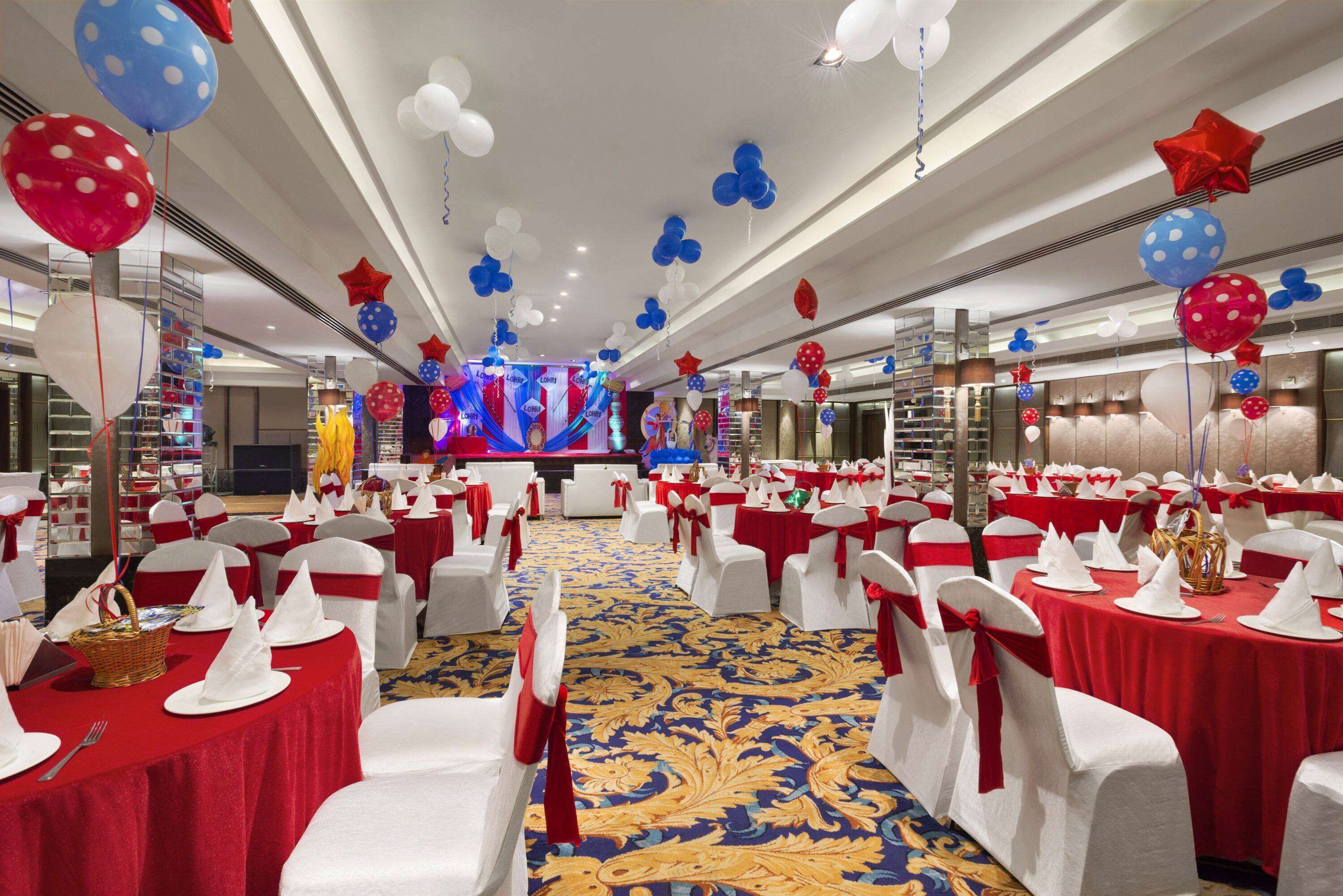 A banquet hall with tables set for a formal event, featuring red and white tablecloths, white chairs with red sashes, and a blue carpet.