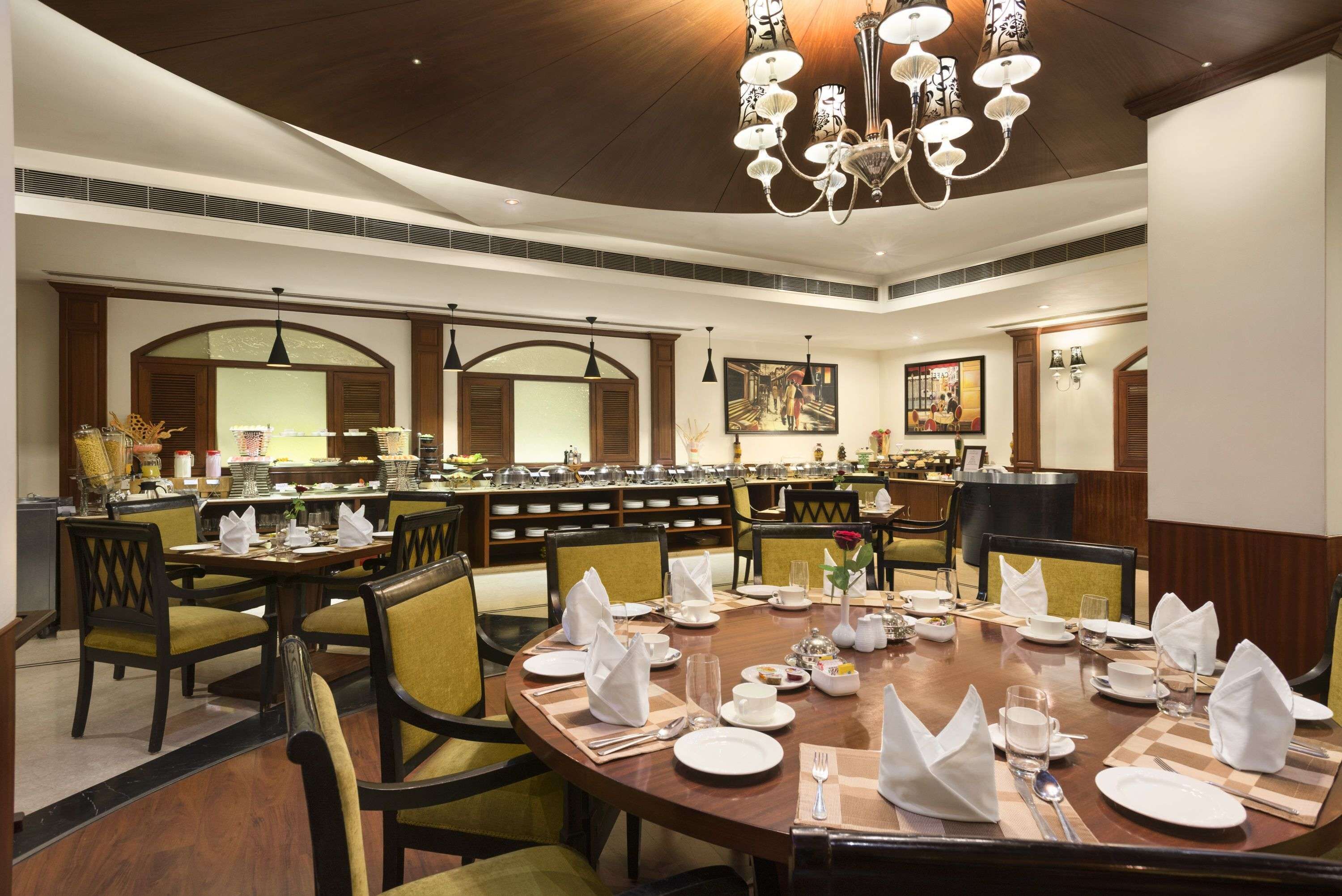 Un espace repas avec des tables rondes disposées pour accueillir plusieurs convives, agrémenté d’un lustre central et d’un buffet en arrière-plan.