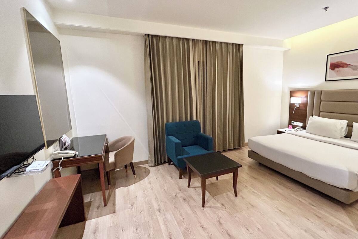 Une chambre d’hôtel avec un lit, un bureau, une chaise, une télévision et une fenêtre avec des rideaux.
