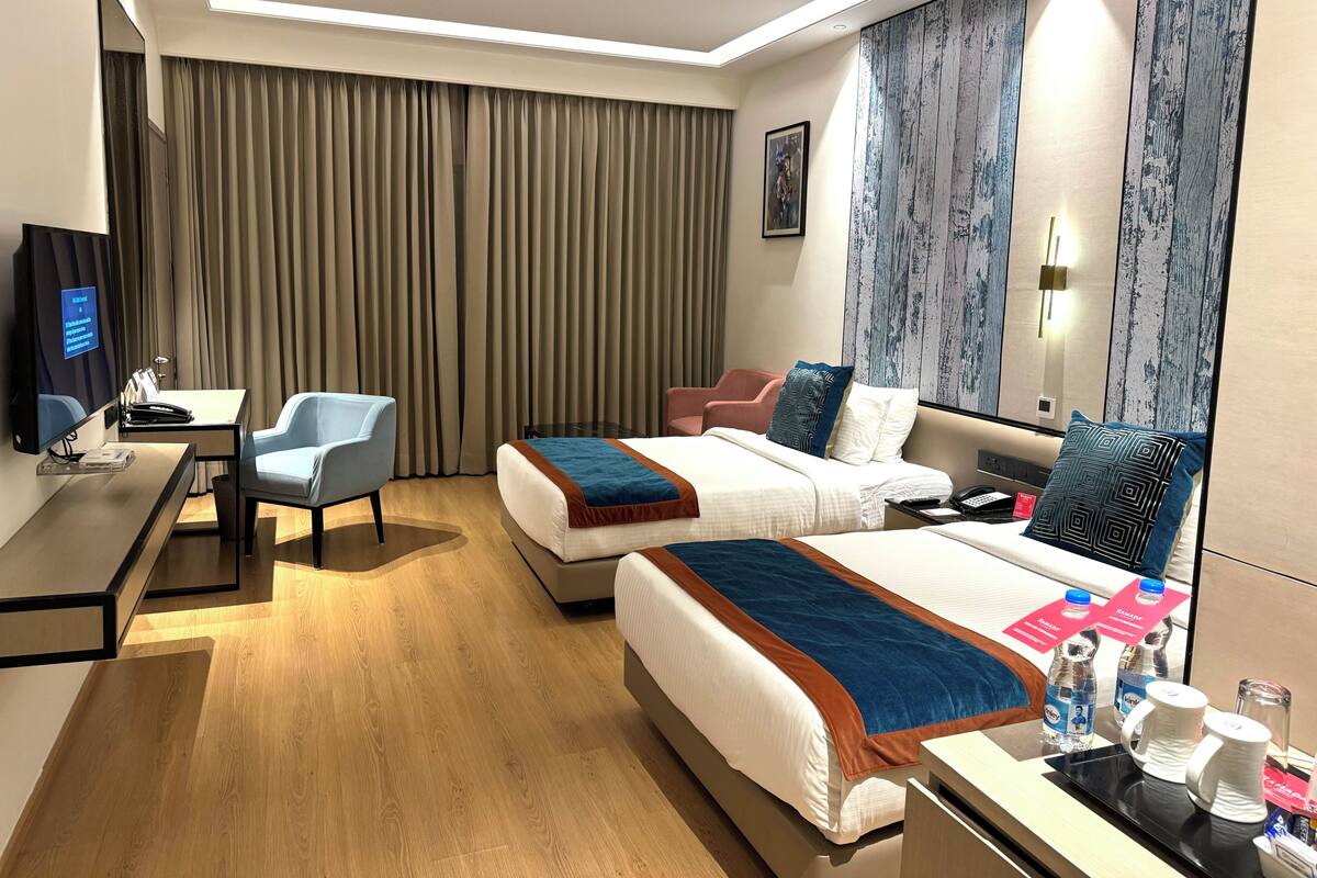 Une chambre d’hôtel avec deux lits, un bureau avec une chaise, une télévision et un grand miroir.