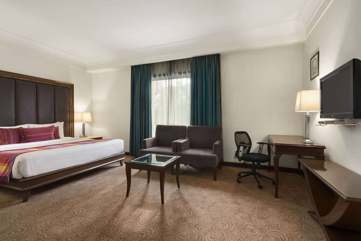 Une chambre d’hôtel comprenant un lit, un canapé, un bureau, une chaise, une télévision et une fenêtre avec des rideaux.