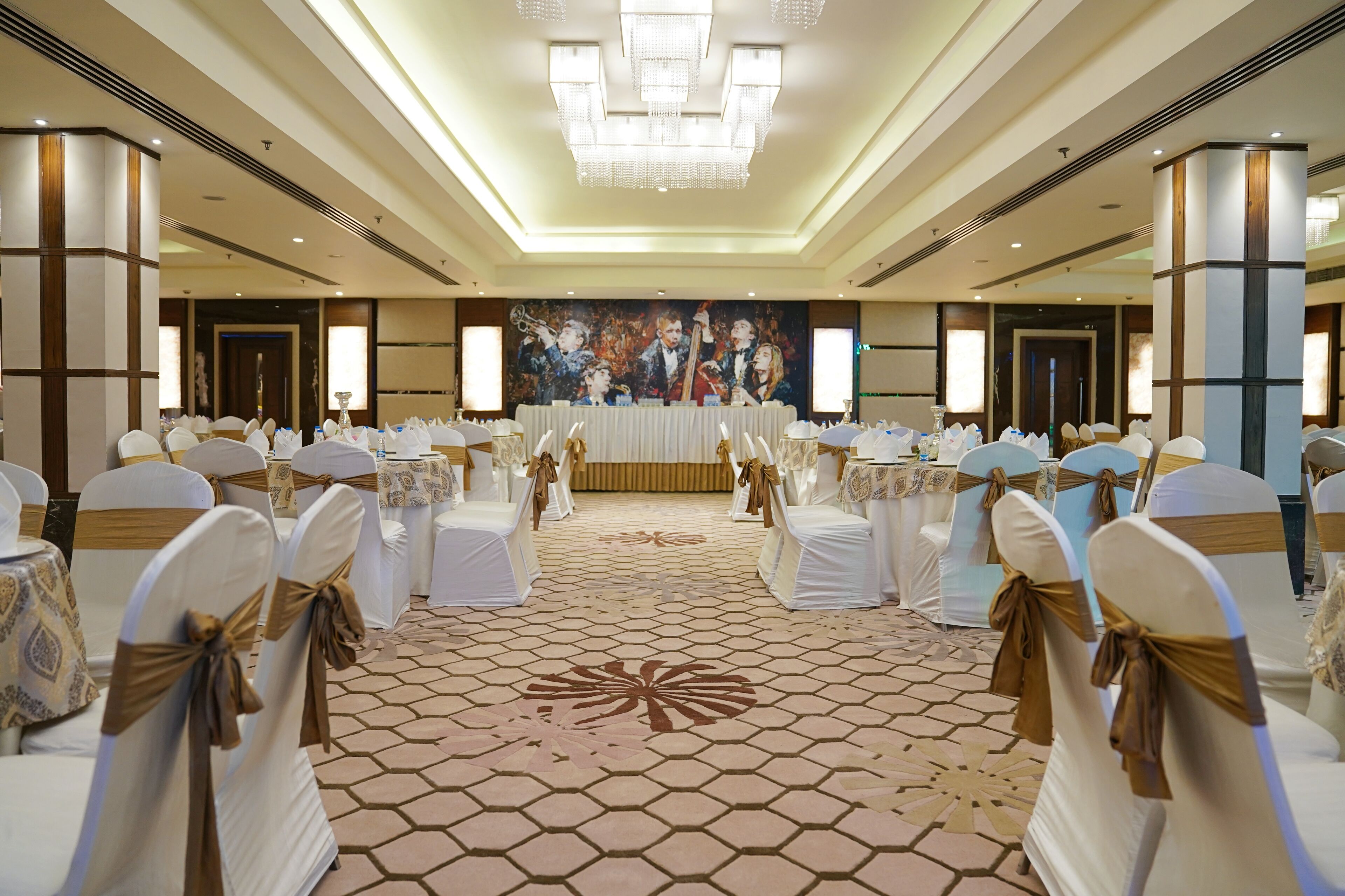Un salón de banquetes con sillas y mesas blancas, un cuadro grande en la pared y una araña.