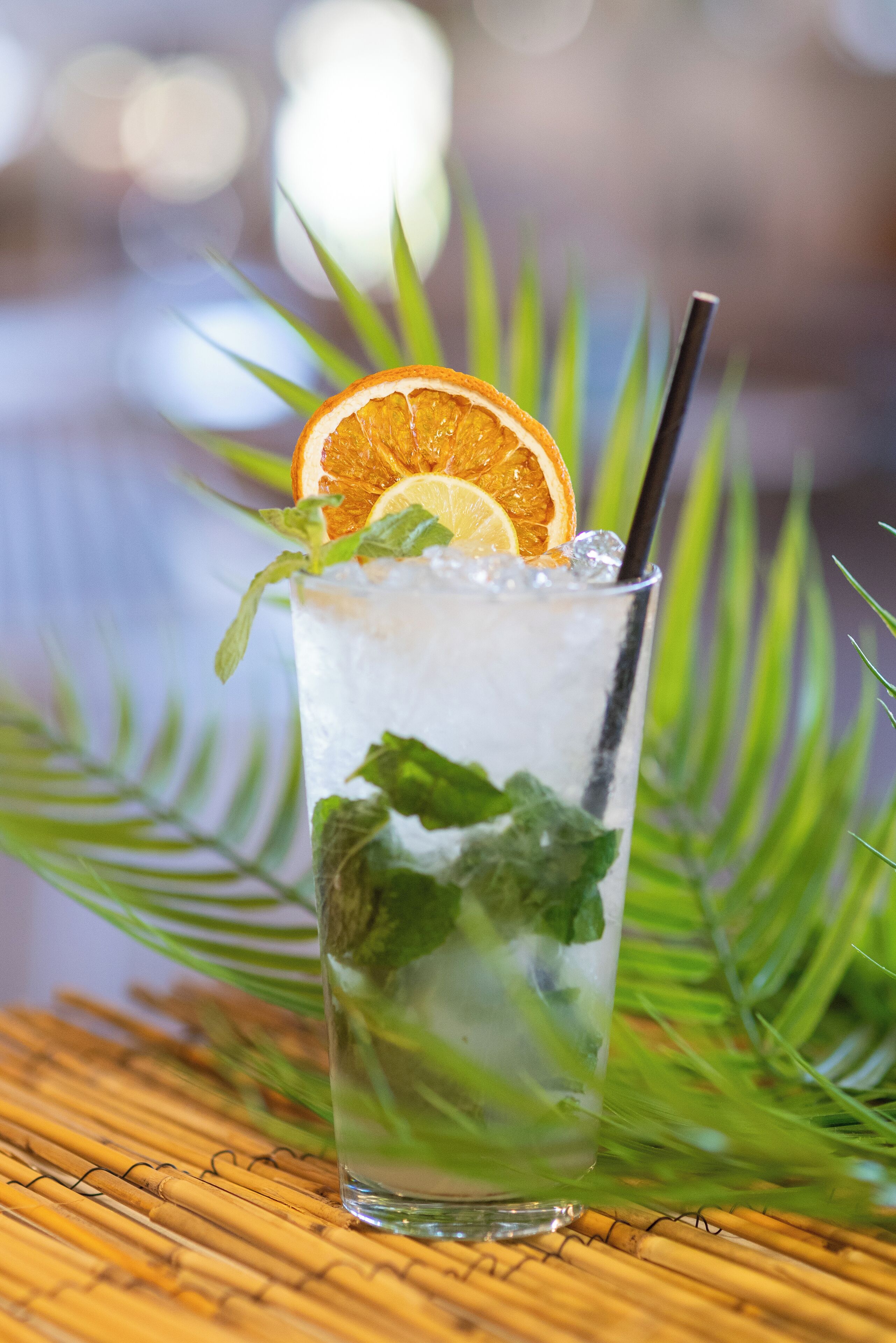 A glass of iced beverage with mint leaves and an orange slice, placed on a bamboo mat.