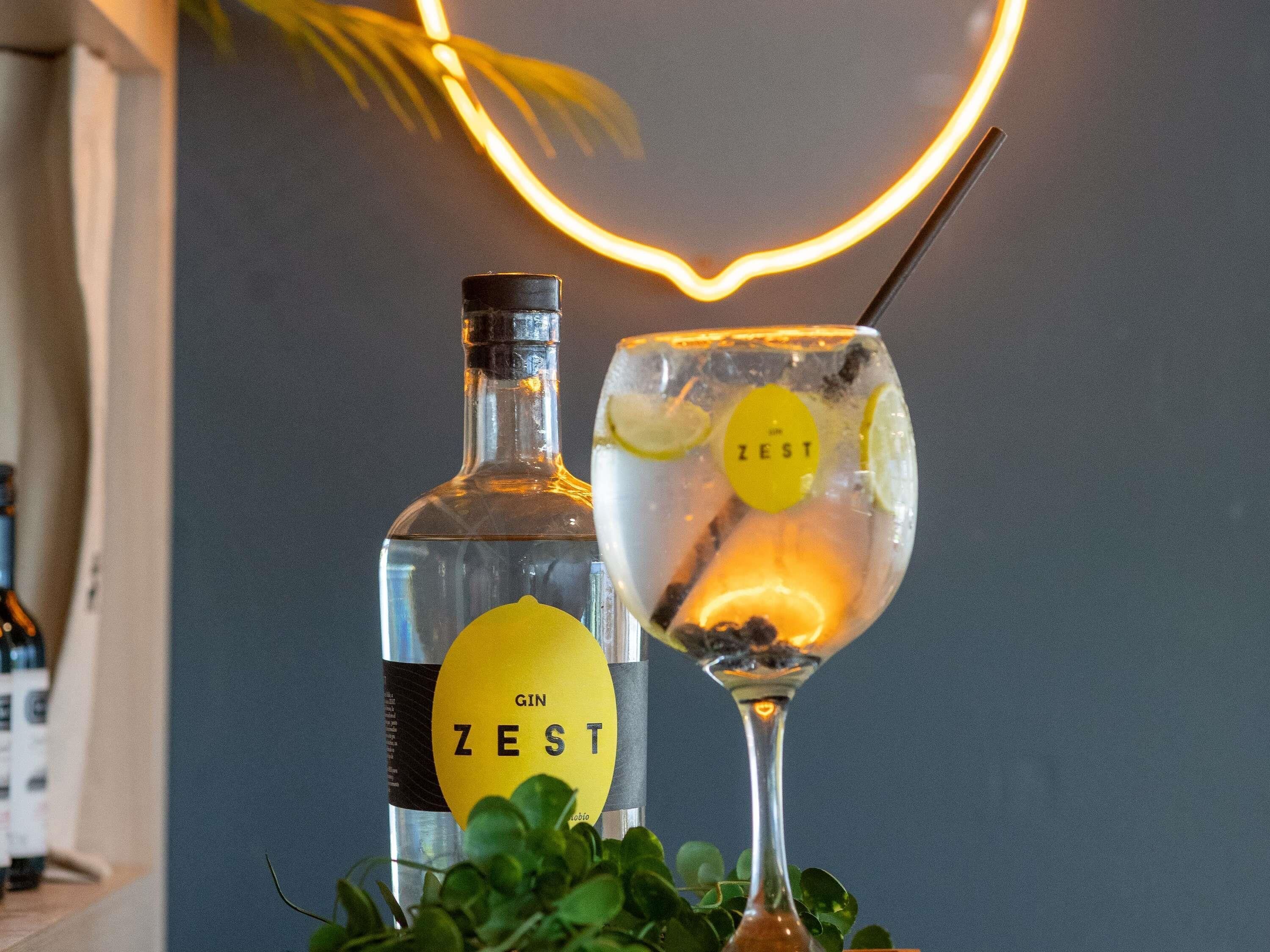 A bottle of gin and a glass with a lemon slice and a straw, both labeled 'ZEST'.