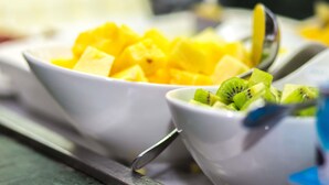 Two white bowls containing diced mango and kiwi on a tray.