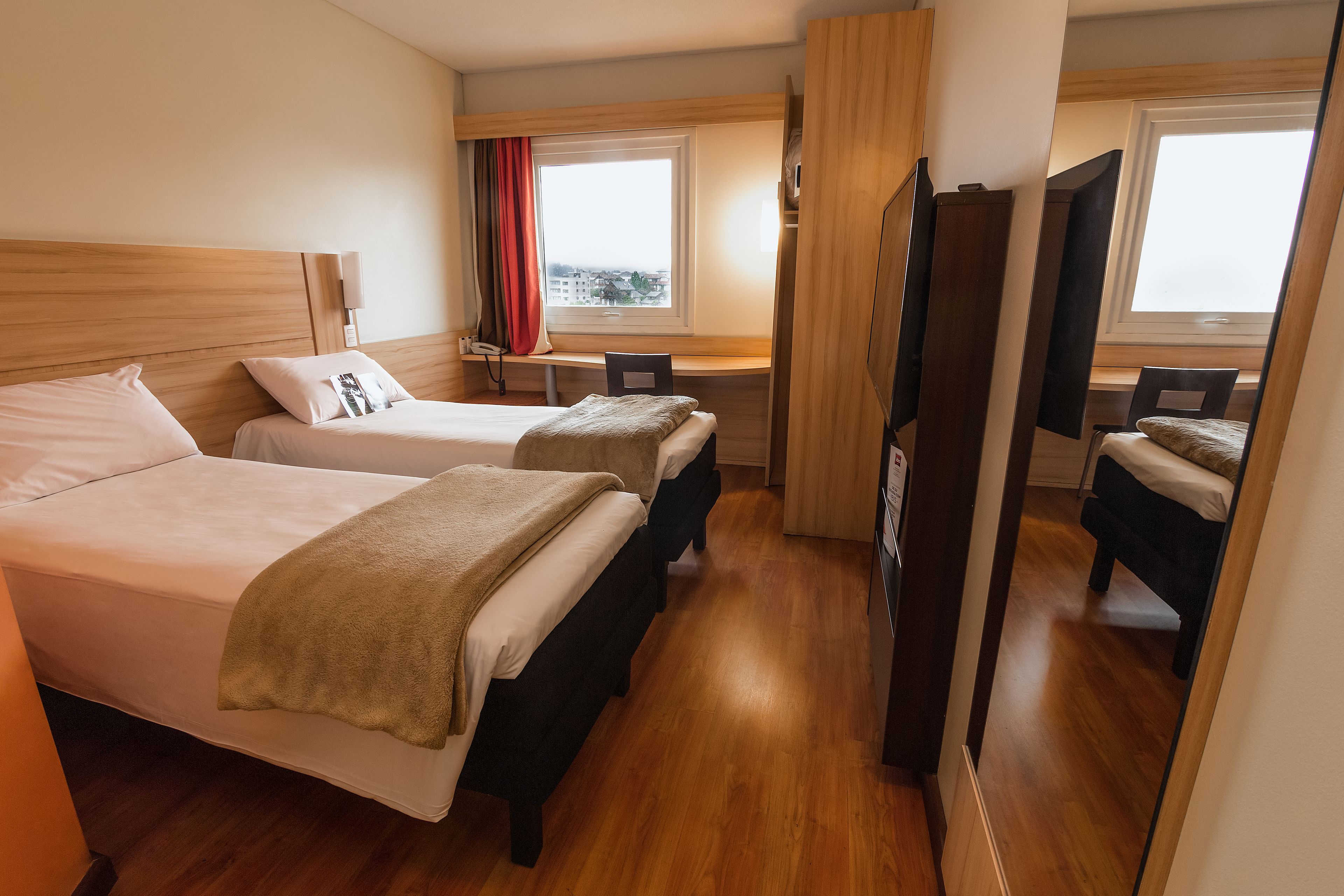 A hotel room with two beds, a desk, a chair, and a TV.