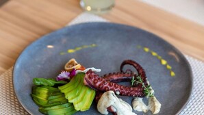 A plate with octopus, avocado, and a small flower on a table.