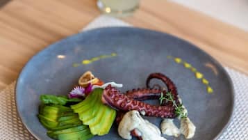 Un plato con pulpo, aguacate y una pequeña flor sobre una mesa.