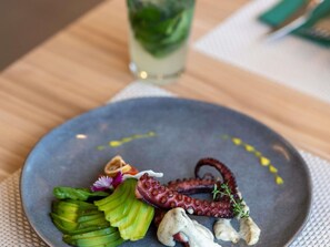 A plate with octopus, avocado, and a small flower on a table.