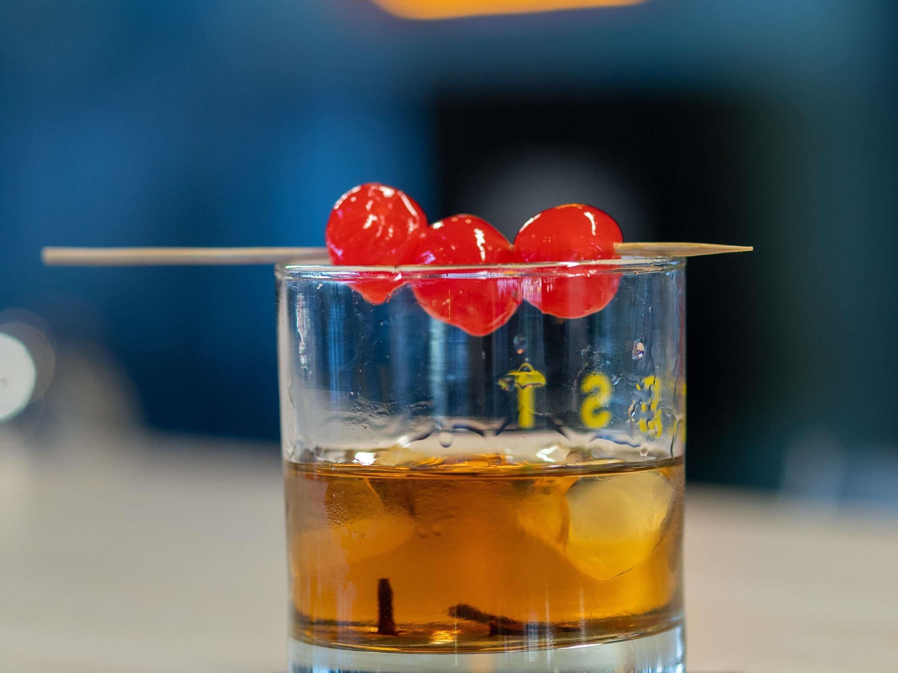 A glass with a clear liquid, ice cubes, and a red heart-shaped garnish.