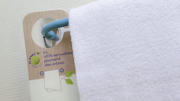 Etiqueta adherida a una toalla con texto sobre la reutilización de toallas para plantar árboles.