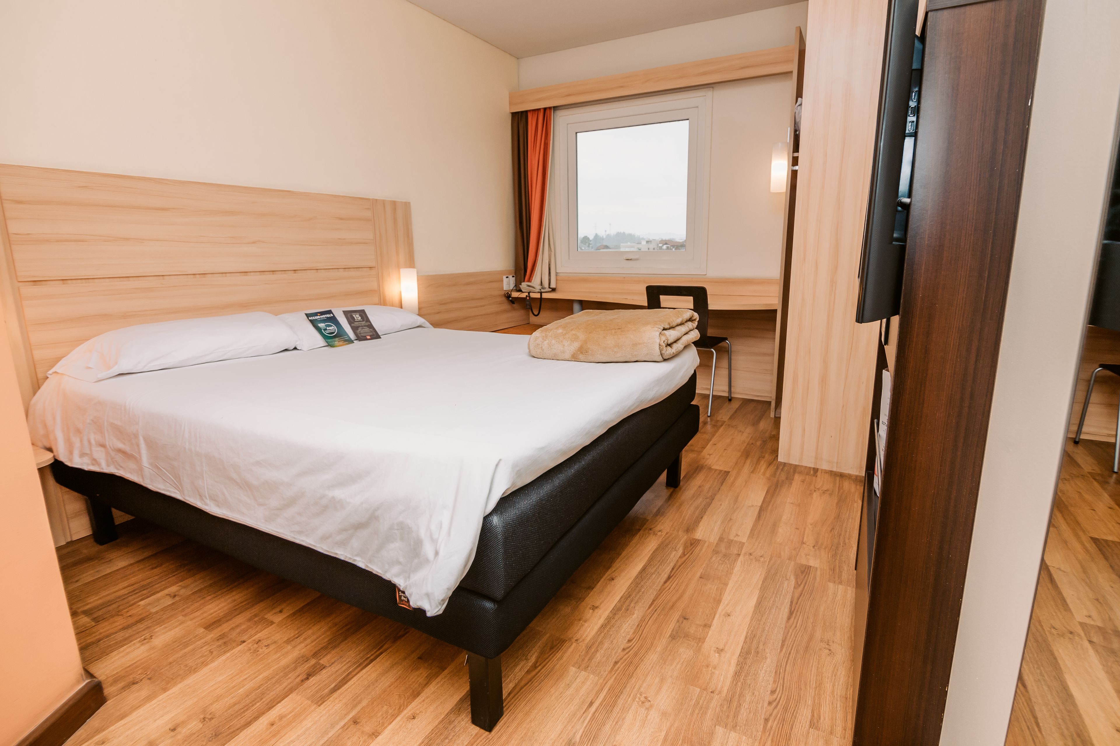 Una camera d'albergo con un letto, una scrivania, una sedia, una TV e una finestra.