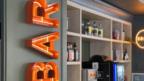Zona de bar con letras de neón iluminadas que dicen "BAR" en la pared, estantes llenos de botellas y una máquina de café.
