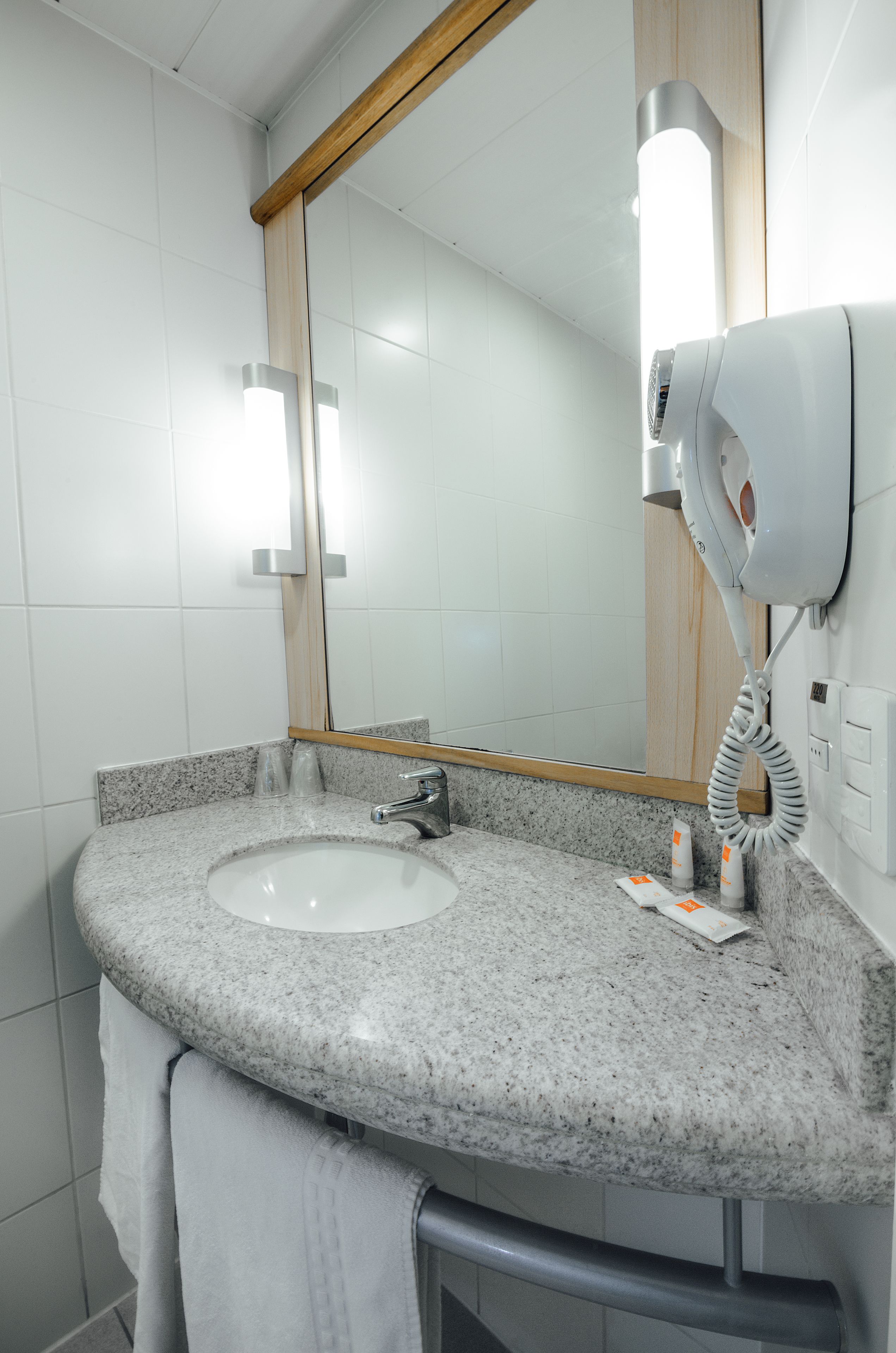 A bathroom with a granite countertop sink, a mirror, a hairdryer, and a towel rack.